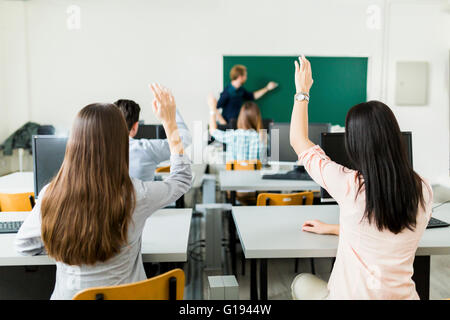 Young students raising hands in a classroom showing they are ready Stock Photo