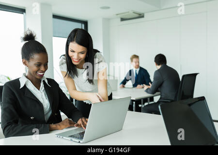 Black and white businesswomen looking at a laptop and working in a neat office environment Stock Photo