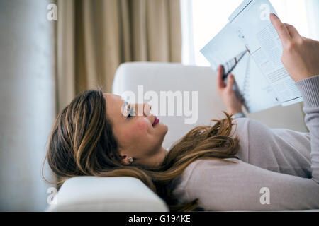 Beautiful woman on a sofa reading a paper in a well lit stylish  living room Stock Photo