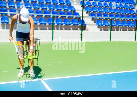 Female tennis player practicing service with the ball basket being at hand Stock Photo