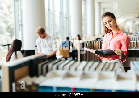 Beautiful woman reading a book in a library and thinking Stock Photo