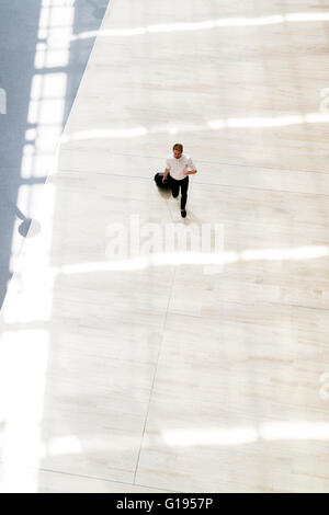 Handsome business holding a trolley and walking in a modern building seen from above Stock Photo
