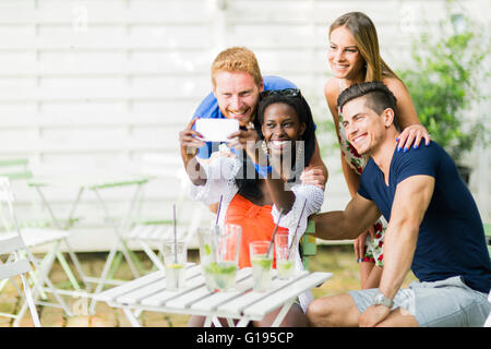 A group of friends sitting a table and talking smiling  while taking selfies on a hot summer day Stock Photo