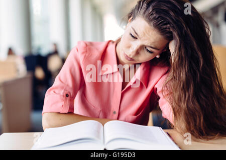 Female student studying and reading in a library but is having a hard time understanding the material Stock Photo