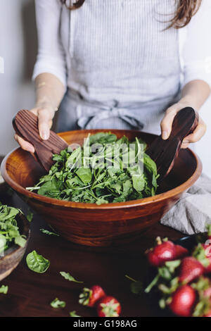 A woman is mixing spinach and arugula to make a strawberry spinach and arugula salad. Stock Photo