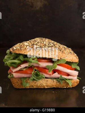 rustic ham salad sandwich in seeded bread roll against dark background Stock Photo