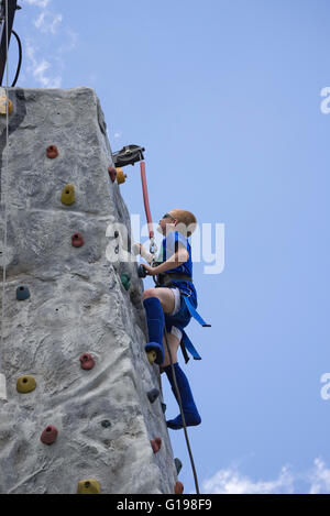 Trying to reach the top of a climbing wall and ring the bell signaling success.  At Pioneer Days annual celebration in High Spri Stock Photo