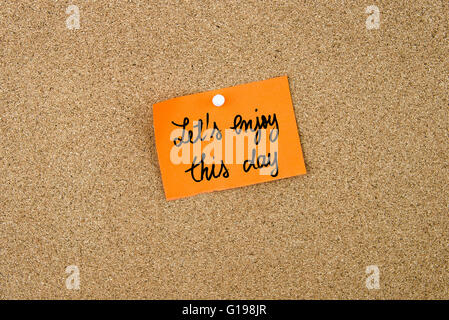 Let's Enjoy This Day written on orange paper note pinned on cork board with white thumbtacks, copy space available Stock Photo