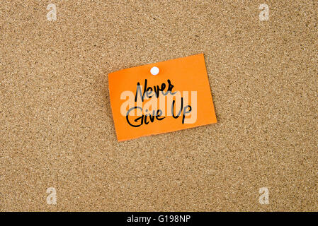 Never Give Up written on orange paper note pinned on cork board with white thumbtacks, copy space available Stock Photo