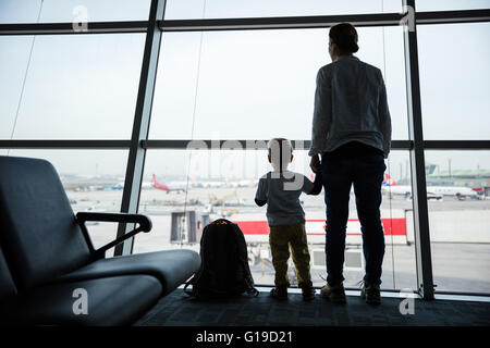 Mother and son standing near window in airport and watching landing field Stock Photo