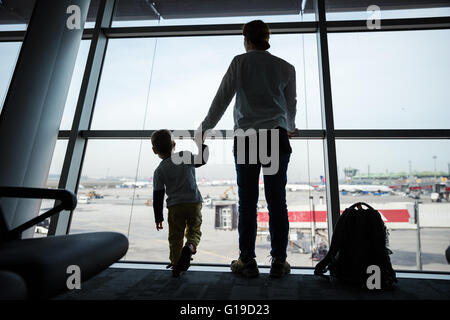 Mother and son standing near window in airport and watching landing field Stock Photo