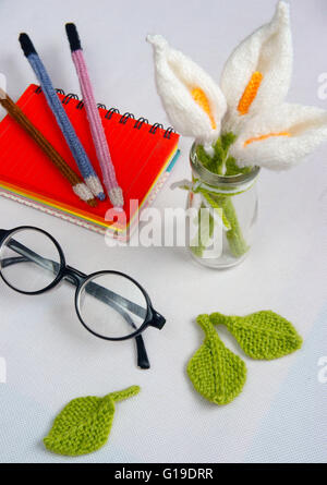 Romantic desk with ornament from handmade product, lily flower knit from white yarn, handbook, knitting pencil, glasses Stock Photo