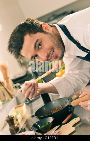 Man happy in kitchen tasting with a wooden spoon in stove Stock Photo