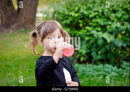 little girl drinks water from a bottle on the nature park Stock Photo