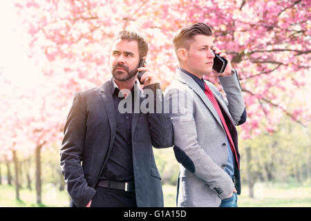 two businessmen standing outside in a park and talking on the phone Stock Photo