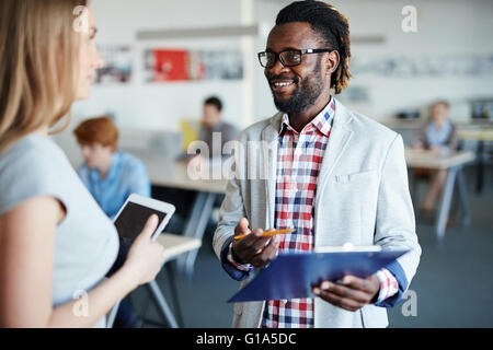 Two young colleagues consulting on background of working people Stock Photo