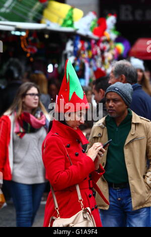 Woman wearing elf costume checks messages on her smartphone in Christmas market, Plaza Mayor, Madrid, Spain Stock Photo