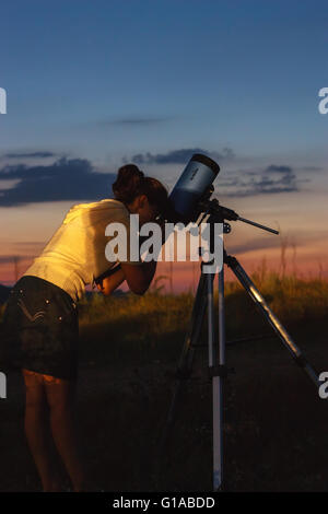 Girl watching through a Skywatcher telescope mounted on a simple equatorial mount pointed to the sky in the evening. Stock Photo