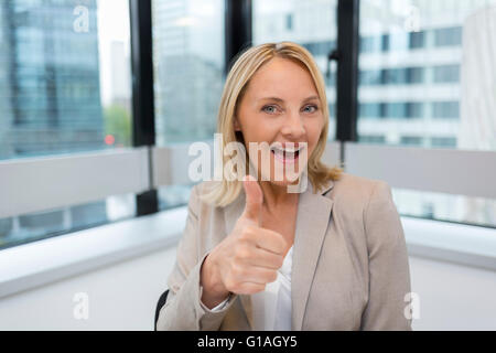 Happy Business woman thumbs up. Modern office background. Looking at camera Stock Photo