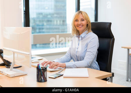 Middle aged business woman working at office on computer. Buildings Background. Looking at camera Stock Photo