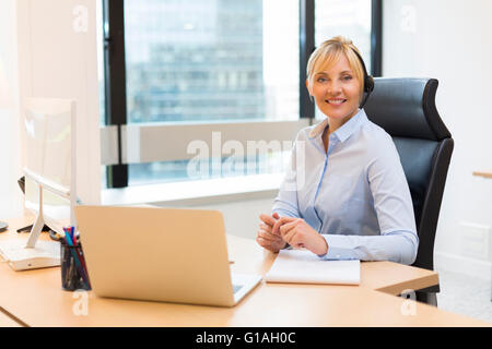 Attractive Business woman working on laptop. Headset. Building background. Looking at camera Stock Photo