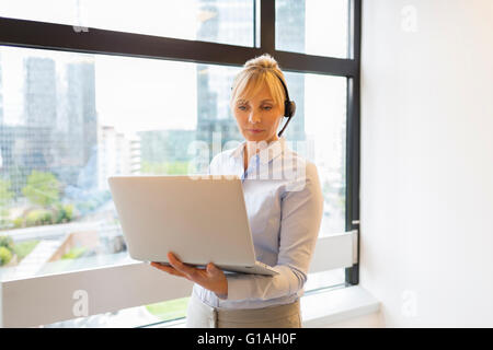 Attractive Business woman working on laptop. Headset. Building background Stock Photo