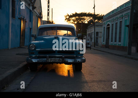An old 1950's US classic car parked on a side street in Cienfuegos with the sun setting behind casting a golden glow underneath Stock Photo