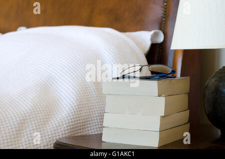 Pile on books with reading glasses on bedside table Stock Photo