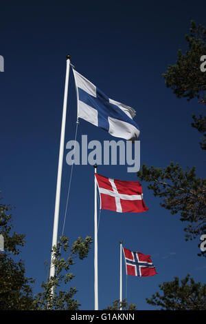 Flags of Finland, Denmark and Norway blowing in the wind on dark blue sky. Stock Photo