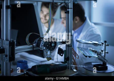 Young engineers working in the laboratory and using a computer, 3D printer on foreground, science and technology concept Stock Photo