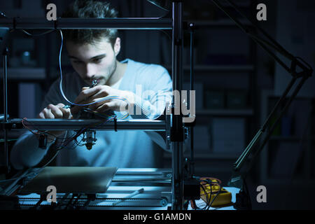 Young engineer working at night in the lab, he is adjusting a 3D printer's components, technology and engineering concept Stock Photo