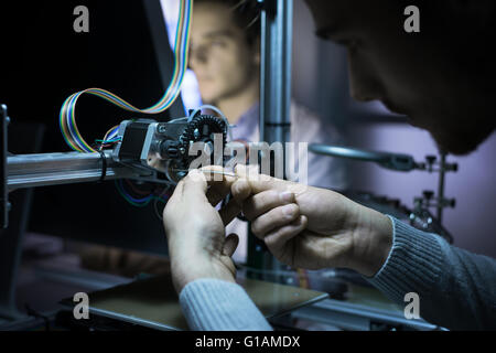 Young engineer in the lab working on a 3D printer, another student is working with a computer on background, innovation and engi Stock Photo