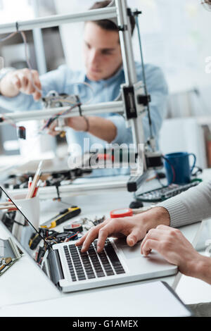 Engineering students working in the lab, a student is adjusting a 3D printer's components in the background, the other one on fo Stock Photo