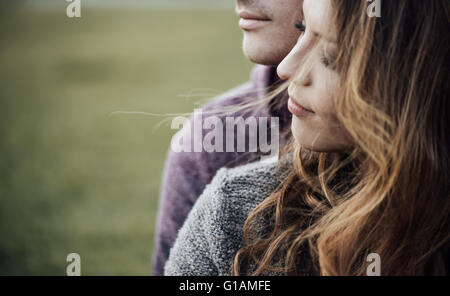Young loving couple outdoors sitting on grass, hugging and looking away, future and relationships concept Stock Photo