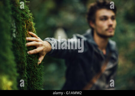 Young man walking in the woods and leaning on a moss covered rock Stock Photo