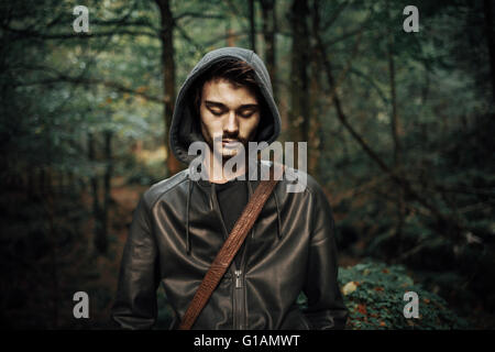 Young hooded cool man in the woods looking down, wild forest on background Stock Photo