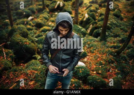 Young hooded cool man in the woods using a mobile touch screen phone Stock Photo