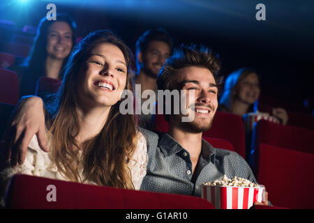 Young loving couple at the cinema watching a movie and smiling, people sitting on background Stock Photo