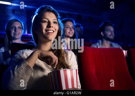 Young smiling woman watching a film in the movie theater and eating popcorn, entertainment and cinema concept