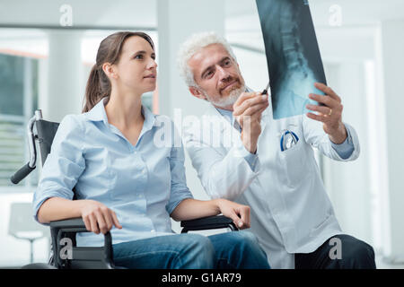 Radiologist examining a woman in wheelchair's x-ray of human spine during a visit at hospital Stock Photo