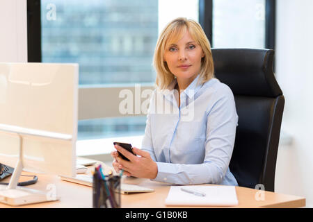 Middle aged business woman working at office. Using smartphone Stock Photo