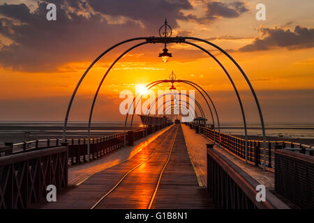 Setting sun over the pier in Southport, Merseyside, UK. May, 2016. UK Weather: Sunset over the pier at Southport after a day of startling temperatures in the north-west of England with 25c being recorded in some areas.  At this time of the year the sun sets almost at the end of the pier giving a perception of the tram lines leading to infinity. Stock Photo