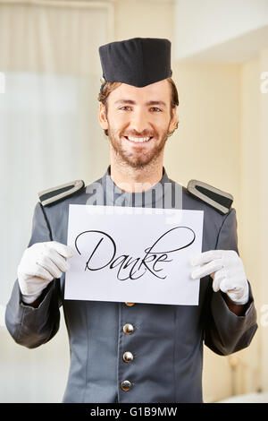 Smiling hotel clerk holding German sign saying 'Danke' (thanks) in hotel room Stock Photo