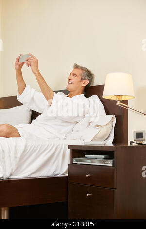 Smiling elderly man in hotel room taking selfie with his smartphone Stock Photo