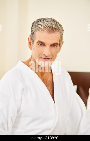 Elderly man sitting in bathrobe on a bed in a bedroom Stock Photo