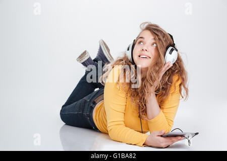 Happy woman in headphones lying on the floor with tablet computer and looking up Stock Photo