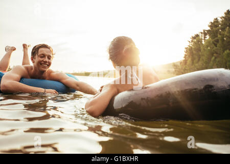 Affectionate young couple floating on inner tubes in water. Young man and woman in an inflatable tube in a lake on a sunny day. Stock Photo