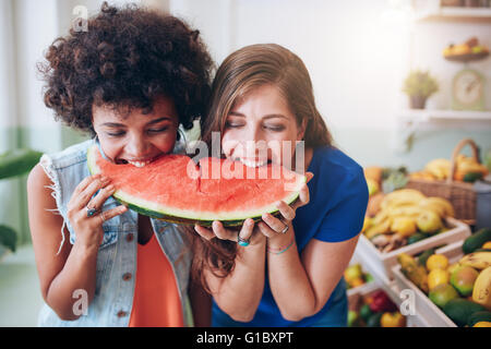 Two young woman eating watermelon and having fun. Mixed race female friends together eating a watermelon slice.