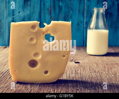 closeup of a piece of Swiss cheese and a glass bottle with milk on a rustic wooden table, against a blue rustic wooden backgroun