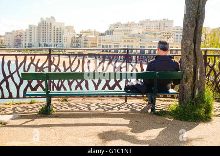 Man reading on bench, view towards Grande Plage, beach, Biarritz, Aquitaine, Basque country, France Stock Photo